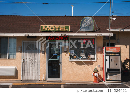 Explore a classic American motel in Barstow on Route 66. Retro neon signs, vintage Coca Cola machine, and nostalgic gas pump create a vintage atmosphere under the sunny desert sky. 114524431