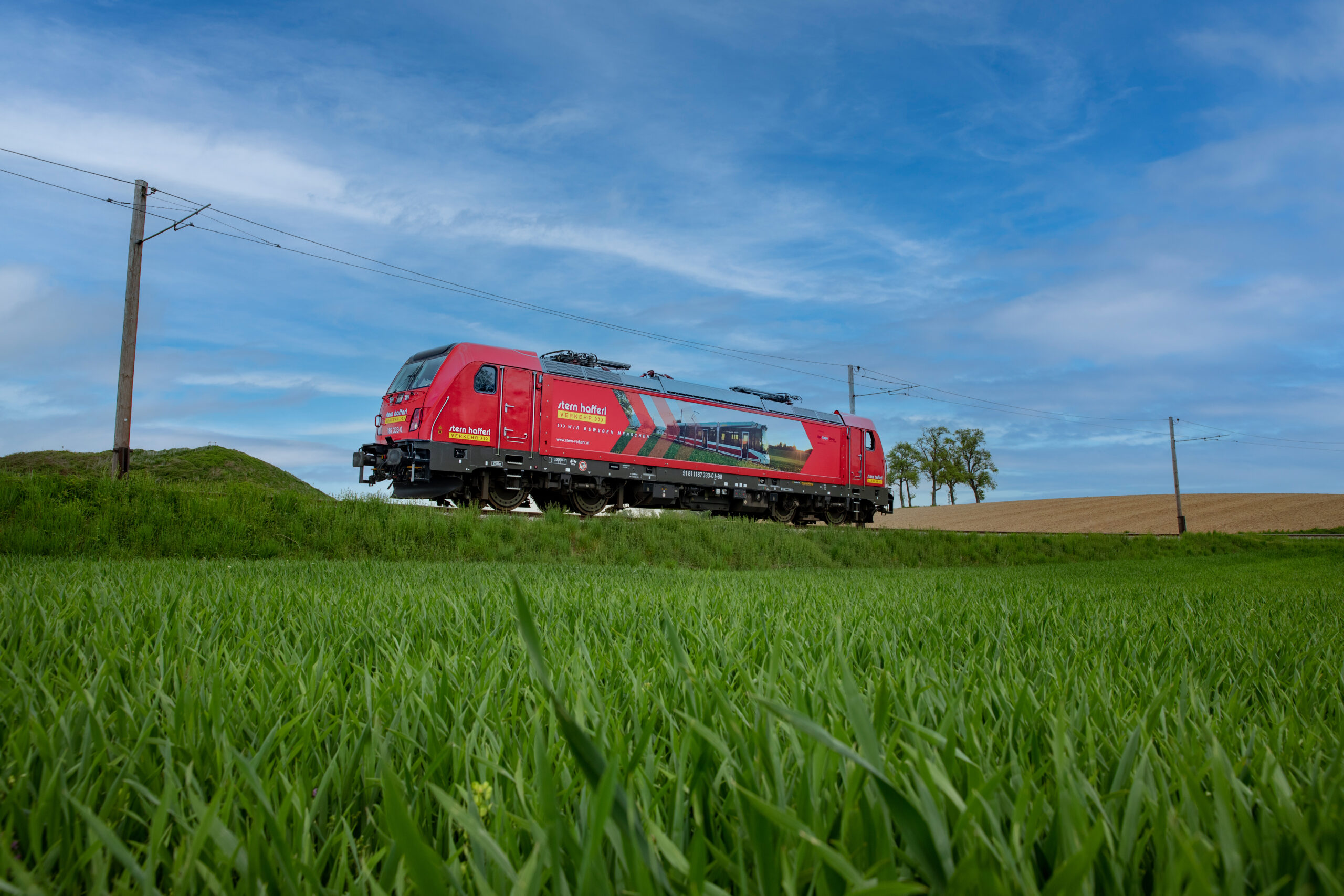 Hybrid Lok Bombardier TRAXX neben einer grünen Wiese