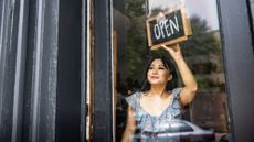 Female small business owner turning around "open" sign on the front door of her store