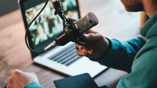 A man host streaming his audio podcast using microphone and laptop at his small broadcast studio, close-up