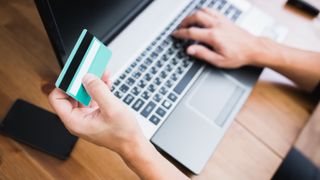 A person holding a credit card in one hand while typing on a laptop keyboard with the other.