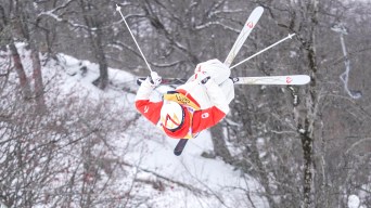 Mik Kingsbury is suspended in midair while wearing a red and white ski suit