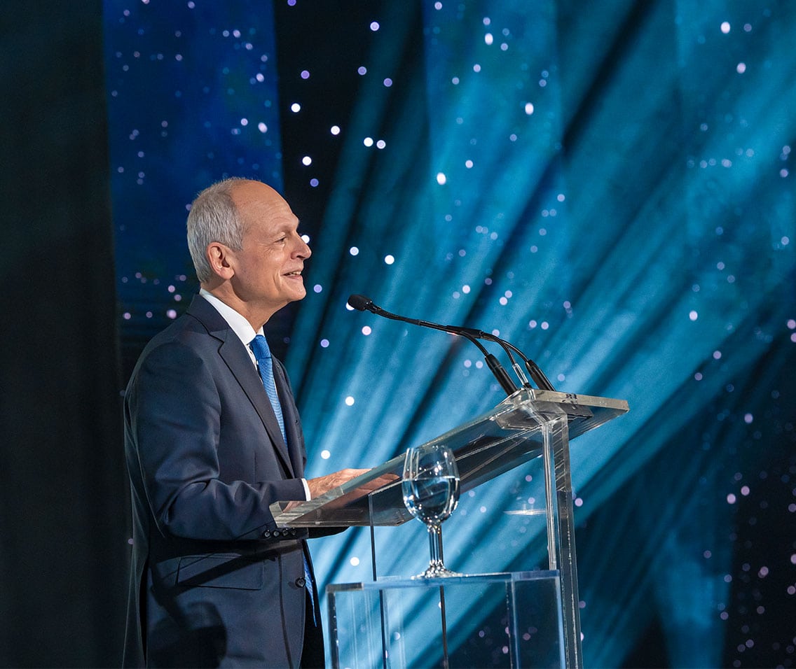 President Meric Gertler standing at a podium with spotlights and twinkling light