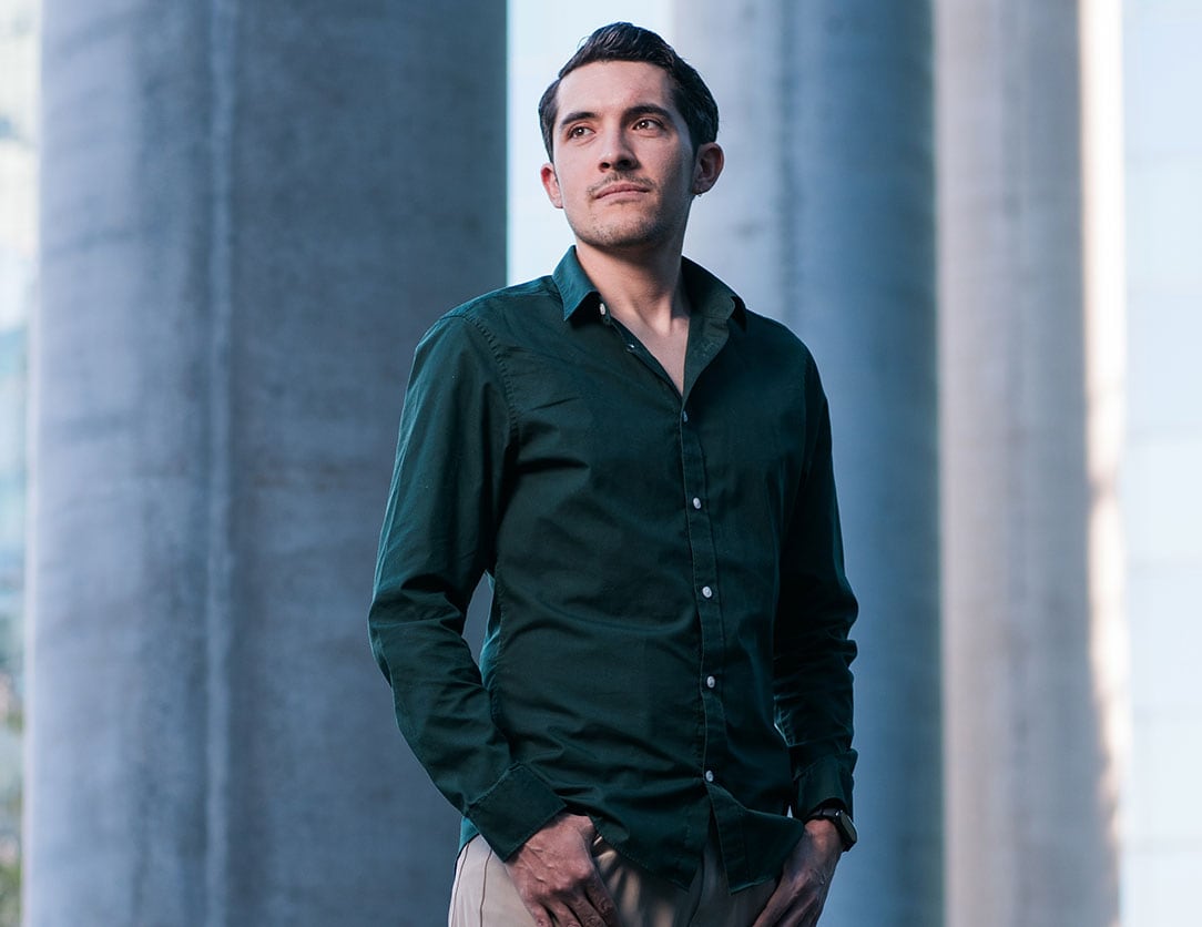 Image of Luis Armando Pérez Dávlaos standing outside of the U of T Nursing building, wearing a white shirt and tan blazer.