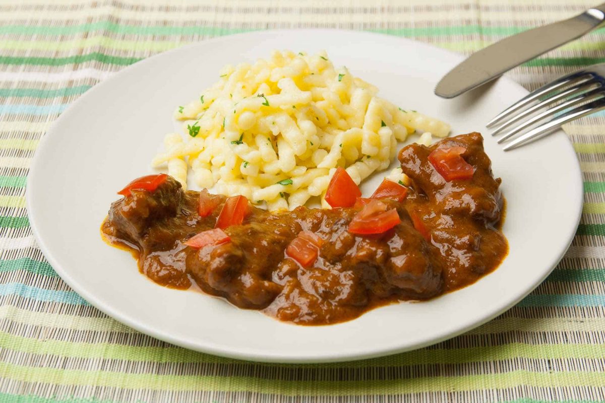 Rindergulasch serviert mit Spätzle, Petersilie und Tomatenwürfel