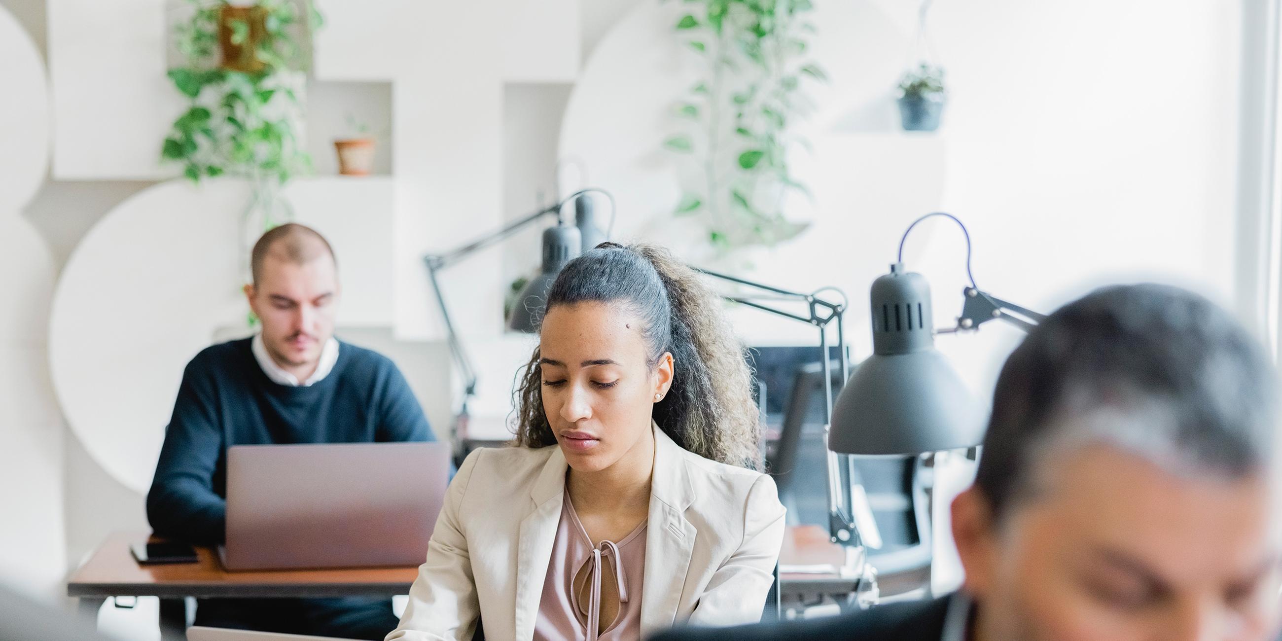 Personen sitzen im Büro und arbeiten an ihren Laptops