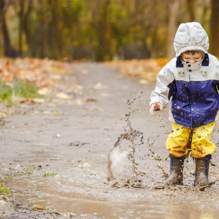 Ein kleiner Junge springt mit seiner Regenhose in einer Pfütze herum. 