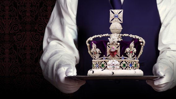 Ein Butler trägt ein Tablett. Darüber schwebt der Sendungstitel "Königliche Etikette – Feinheiten des royalen Protokolls". © NDR/picture alliance/colourbox/M. Stolt Chromorange/Nino Pkhaladze 