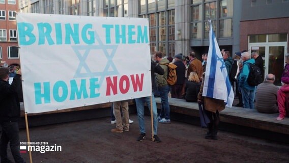 Ein Schild mit der Aufschrift "Bring them home now" von der Mahnwache in Lübeck. © Screenshot 