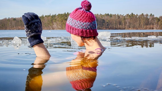 Eine Frau mit Wollmütze und Wollhandschuhen beim Eisbaden. © Colourbox Foto: -