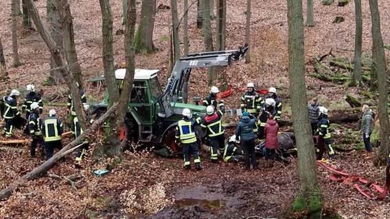 Ein Traktor steht in einem Wald, um diesen herum mehrere Einsatzkräfte der Feuerwehr © NDR Foto: NDR Screenshot