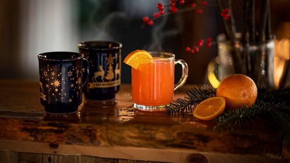 Zwei Tassen mit Glühwein und ein Orangen-Punsch stehen auf einem weihnachtlich geschmückten Tisch. © picture alliance / Zoonar Foto: Marco Martins