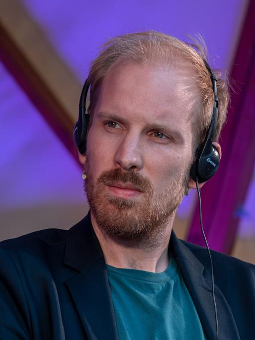 Der niederländische Historiker und Autor Rutger Bregman hört mit einem Headset aufmerksam der Übersetzung einer Rede in Barcelona zu.