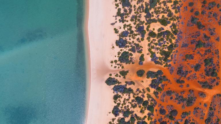 Luftaufnahme eines Strandes in Australien. Durch die Färbung des Wassers und der Wüste, ähnelt die Aufnahme Klimastreifen.