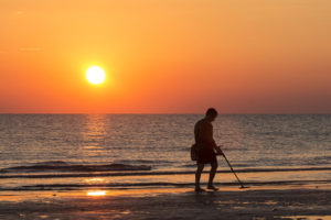 Mann mit Metalldetektor am Strand im Sonnenuntergang