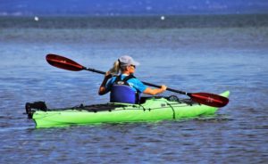 Frau fährt Kajak mit Schwimmweste und Sonnenschutz