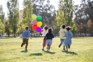 Kinder rennen mit bunten Luftballons auf einer Wiese