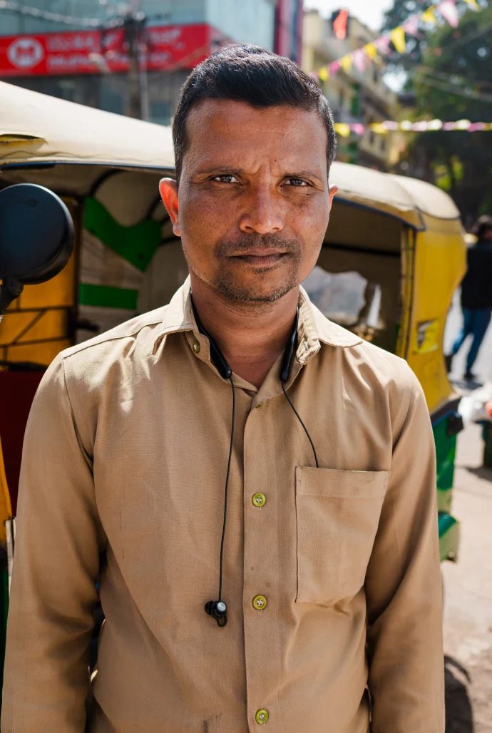  Indian man standing in the sun in a tan button-up shirt.