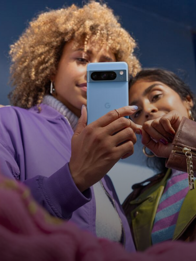 A pair of Android users look at a phone.  One of the users points to a text message response on the screen.