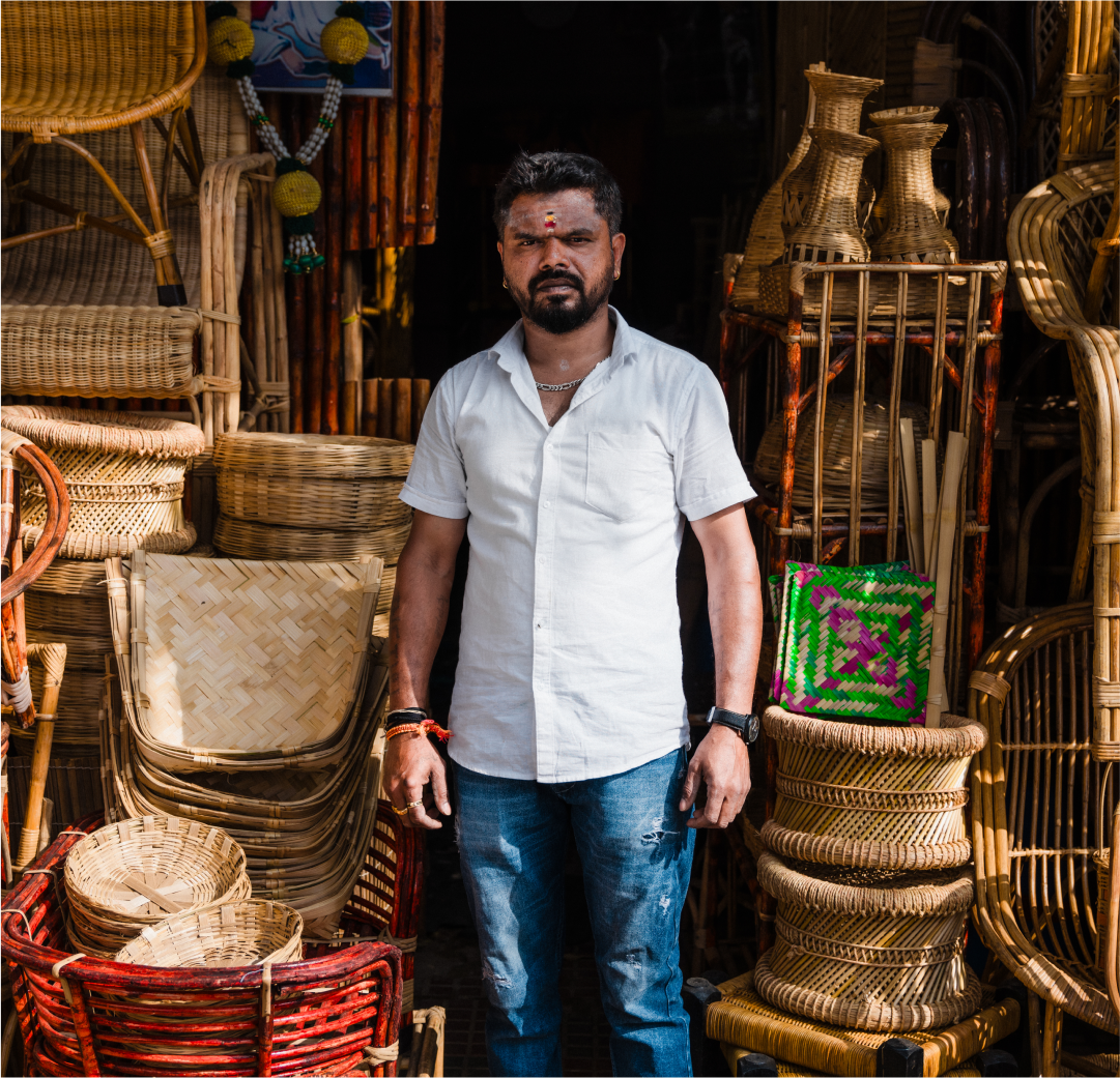 South Asian man in a white collared shirt, standing in front of a pile of baskets.