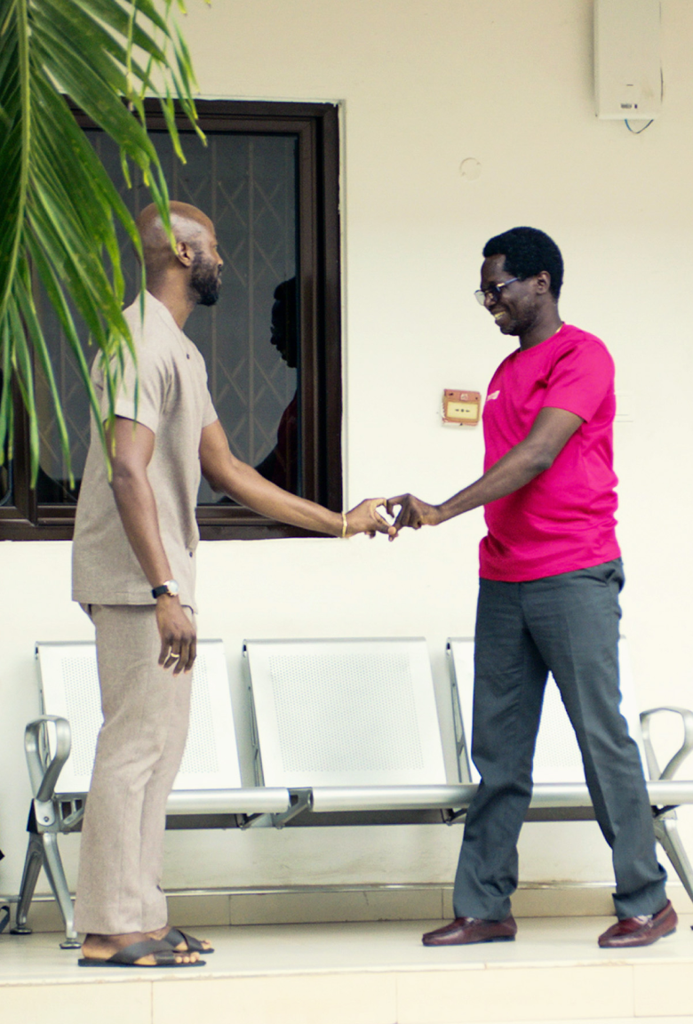 Two Ghanaian men reach out in front of them to shape a heart with their fingers.