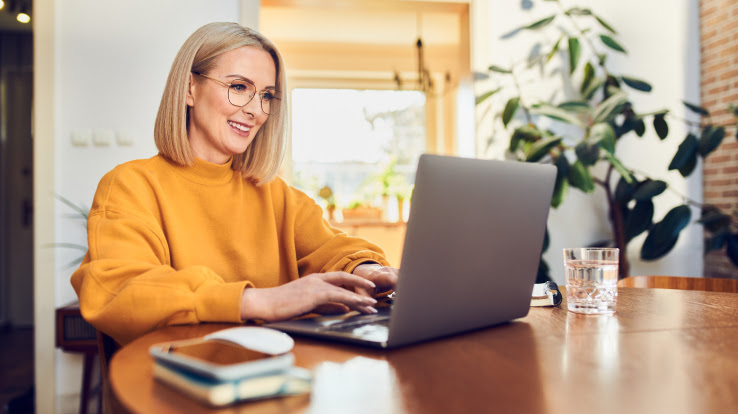 Perempuan sedang bekerja di rumah menggunakan laptop. 