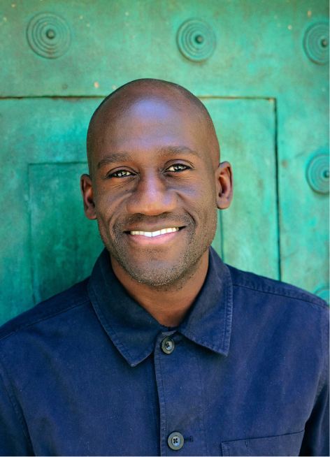 A Black man smiling in a blue collared shirt.