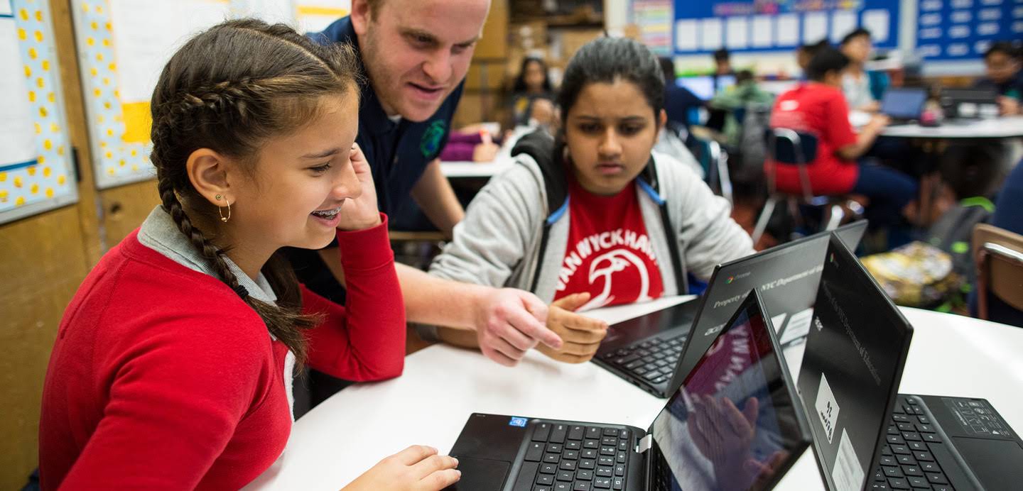 Teacher helps two students on Chromebooks.