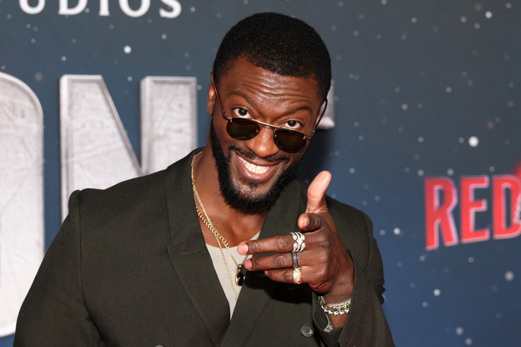 Aldis Hodge, dressed in a suit and sunglasses, pointing at the camera at the New York premiere of Amazon MGM Studios' 'Red One'