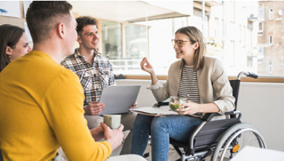 Jovens funcionários participando de uma reunião no escritório com uma mulher sentada em uma cadeira de rodas.