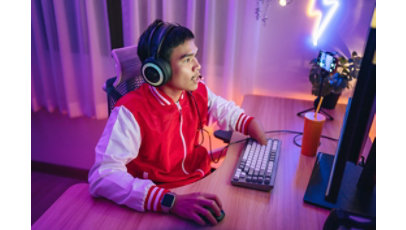 A male gamer with a physical disability is wearing a headset and playing online games in a neon-lit room.