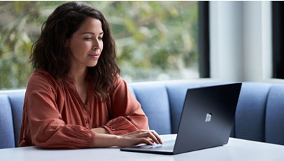 A businesswoman working on a laptop at a table by a window.