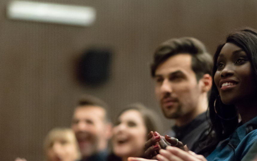 People in an audience applauding in a theater.