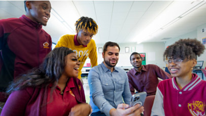 Young people react with excitement while a teacher looks at a mobile phone.