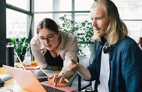 Colleagues collaborate over a laptop in an office environment.