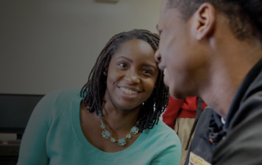 Two people in a computer lab smile at each other.