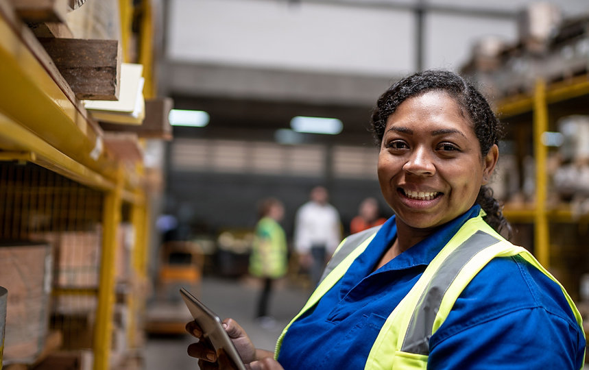 A woman in a warehouse setting holding a tablet.