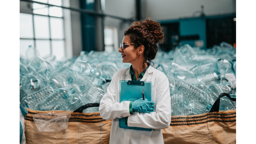 Woman standing in front of bin full of empty plastic bottles.