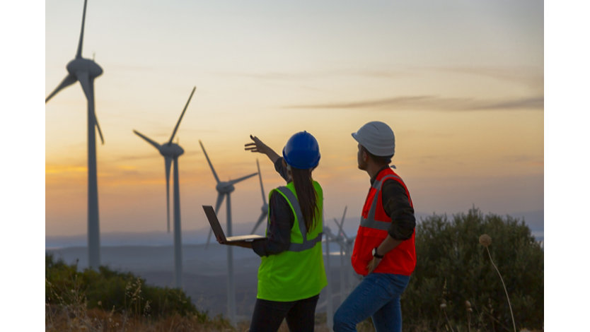 Two energy workers out in the field looking at wind turbines.