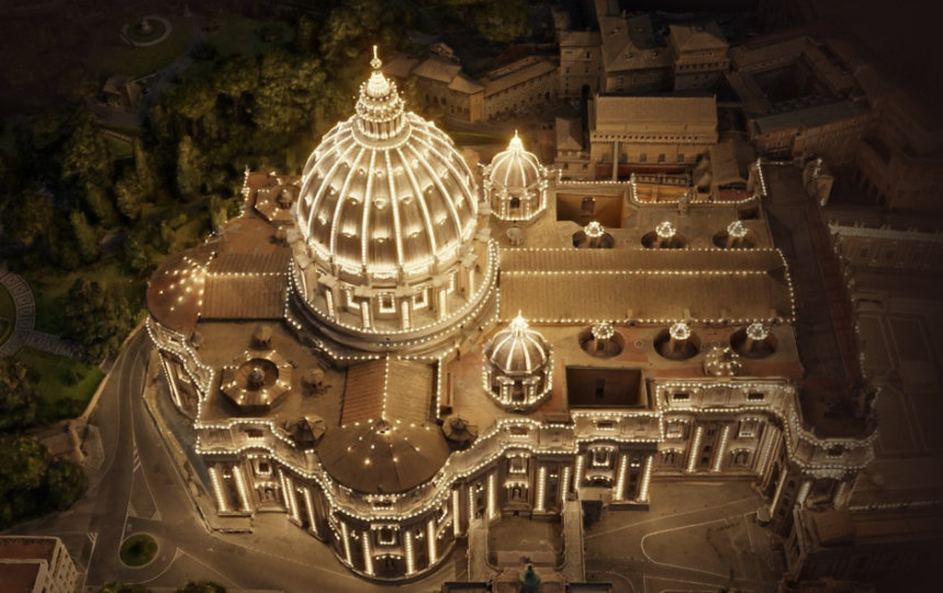 An aerial view of the dome of St. Peter's Basilica with lights outlining major structures.