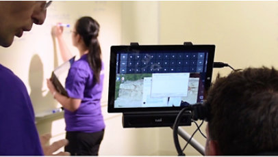 Someone appears to use eye tracker while a woman writes on a whiteboard.