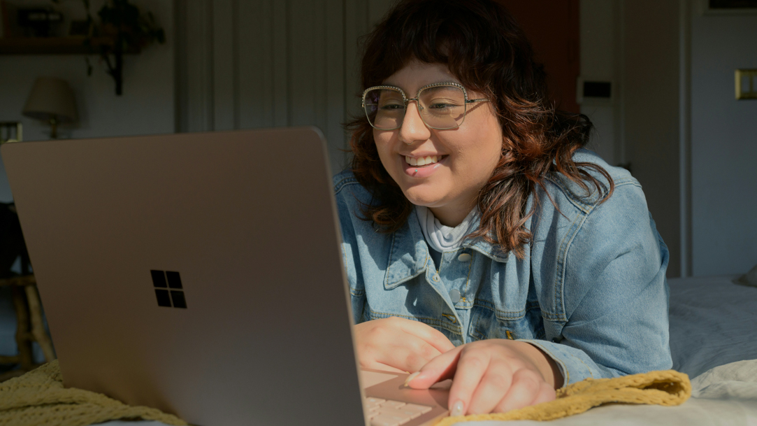 A girl who’s smiling and using a gold Surface laptop