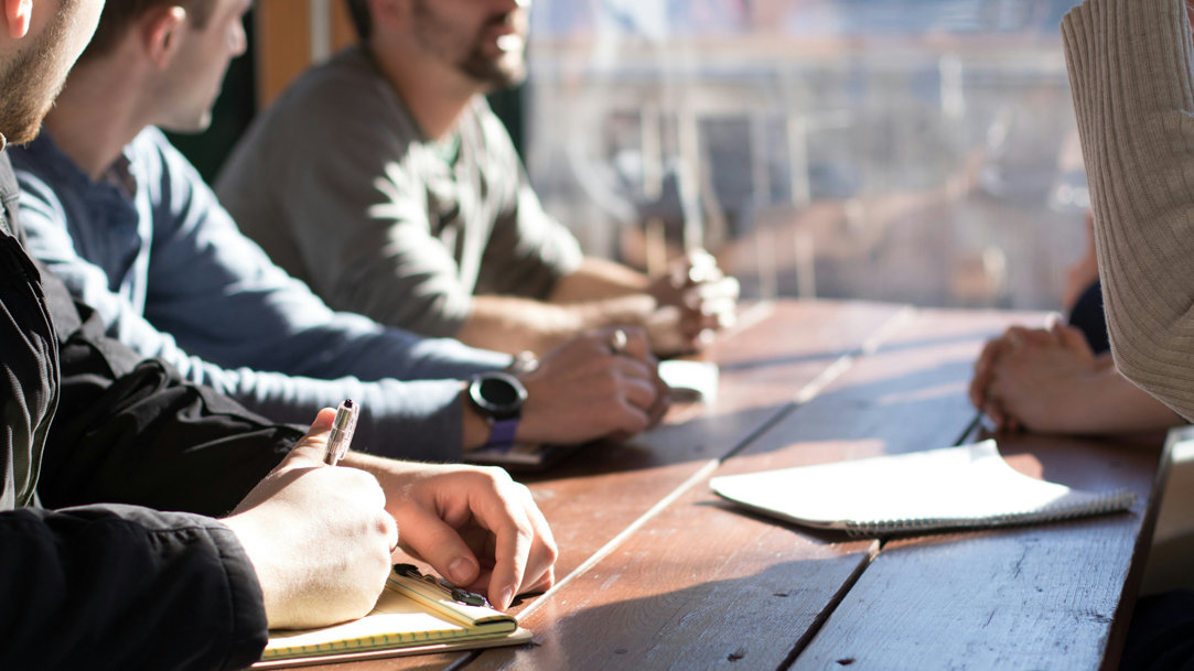 A group of people sitting at a table, talking, and writing notes