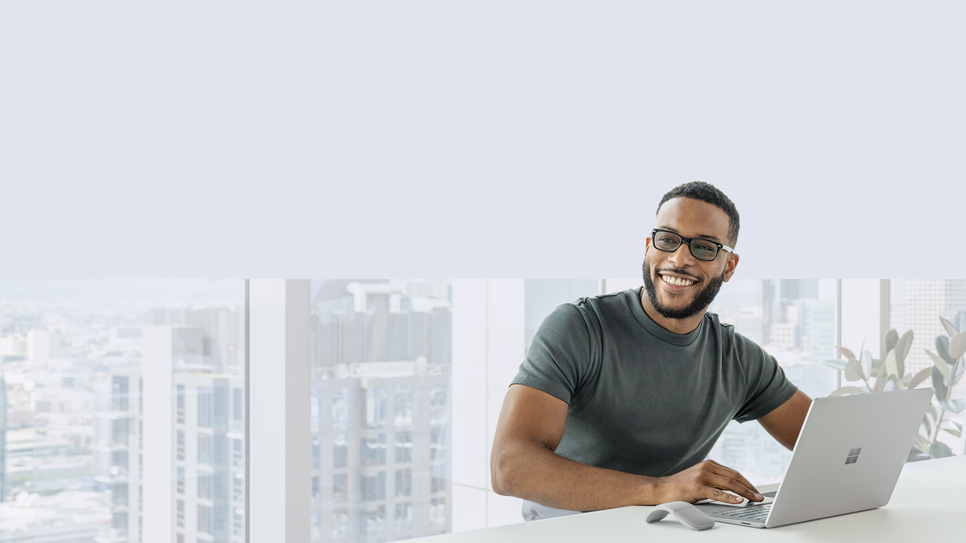 A man sits at his Surface Laptop 5 while looking off into the distance