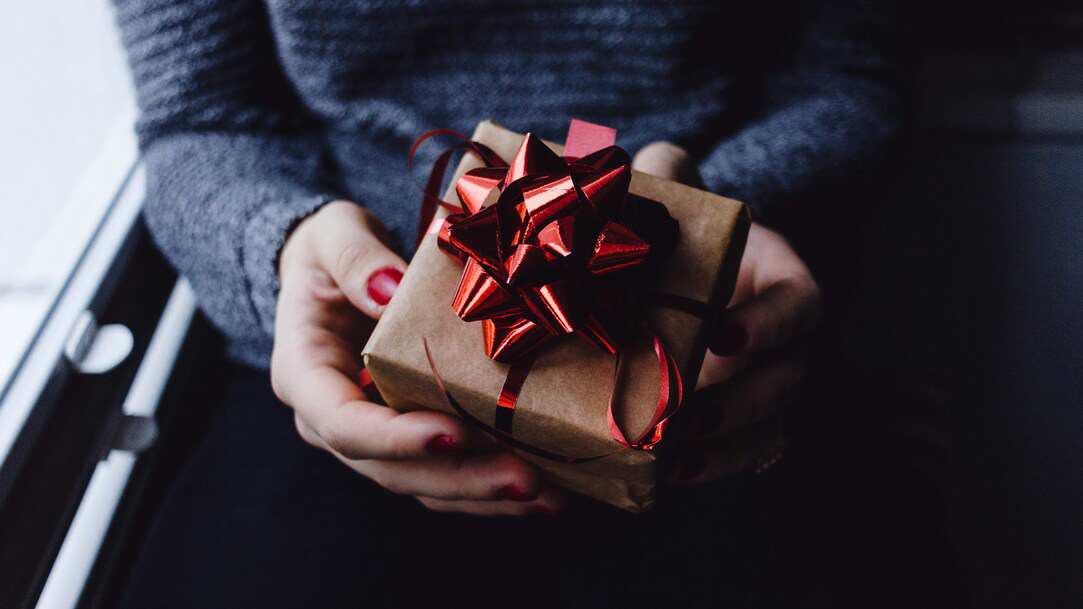 A person holds a box wrapped in brown butcher paper with a shiny red bow on top