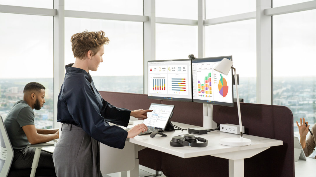 A person working on a Surface device with two monitors in glassy office