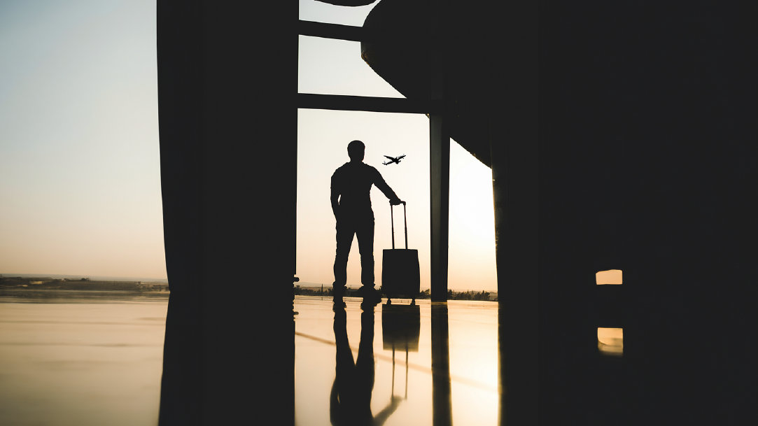 A silhouette of a person with a suitcase looks at an airplane taking off