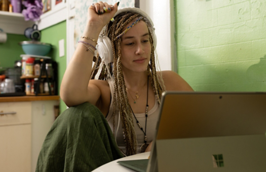 A woman with braids sitting in front of a laptop computer with headphones on