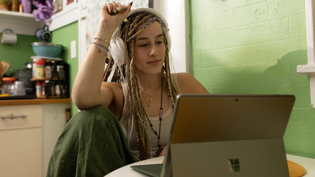 A woman with braids sitting in front of a laptop computer with headphones on