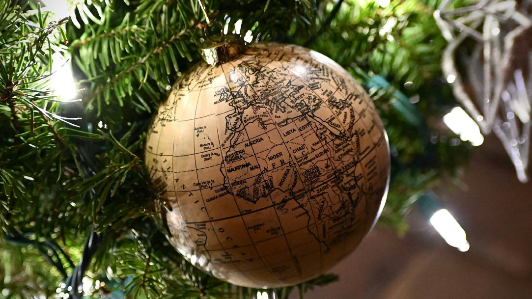 An image of an ornament depicting the world globe and hanging on the branch of a Christmas tree